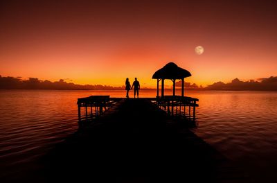 Silhouette pier on beach against orange sky