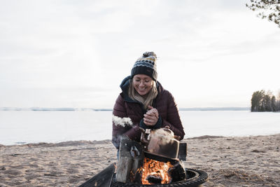 Woman smiling warming up by a camp fire on the beach in winter