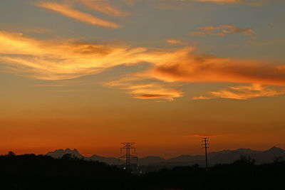 Silhouette electricity pylon against dramatic sky during sunset