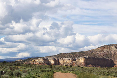 View of dirt road along rocky mountains against cloudy sky