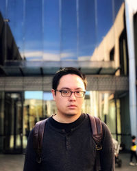 Portrait of a young man wearing eyeglasses against reflective glass facade.
