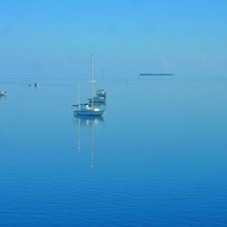 Boats sailing in sea against clear blue sky