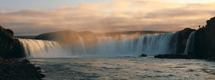 Scenic view of waterfall against cloudy sky at sunset