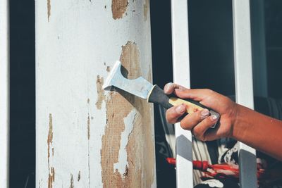 Cropped hand of man scraping paint on wall at home