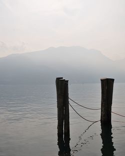 Wooden posts in sea against mountains and sky