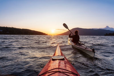 People in sea against sky during sunset