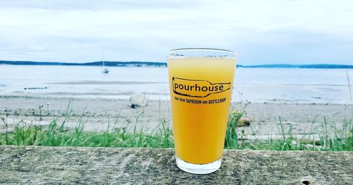 Close-up of yellow drink by glass on beach against sky