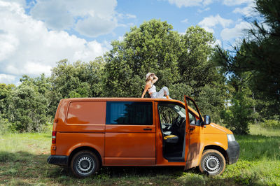 Low angle of serene female explorer sitting on roof of van and enjoying summer adventure on sunny day