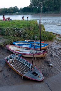 Boats moored on river by trees against sky