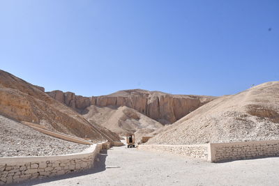 Road leading towards mountains against clear blue sky