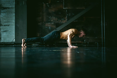 Shirtless muscular man practicing push-ups on floor