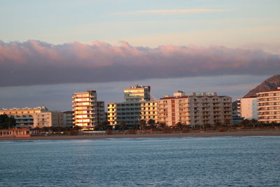 Sea by buildings against sky during sunset