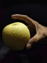 Close-up of hand holding pear against black background