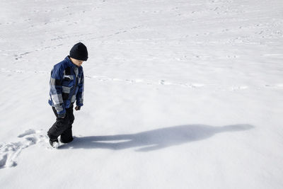 Full length of boy wearing warm clothing while walking on snow covered land