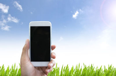 Cropped hand of person holding smart phone on field against sky