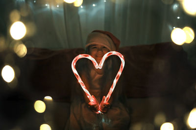 Girl making heart shape of illuminated candy canes on sofa in darkroom