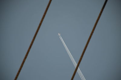 Low angle view of airplane flying against clear sky seen amidst cables