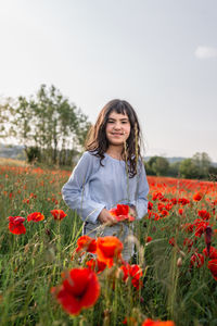 Portrait of young woman standing amidst flowering plants on field against sky