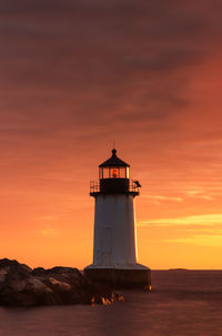 Lighthouse by sea against sky during sunset