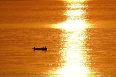 Silhouette people on boat in sea against orange sky