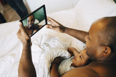 Smiling father and daughter taking selfie on digital tablet while lying in bed at home