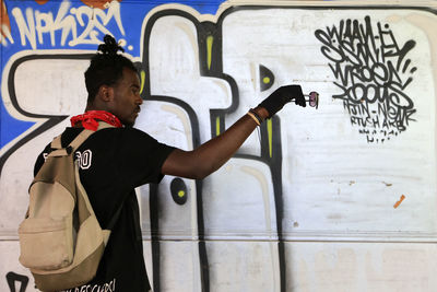 Man holding sunglasses and standing against wall with graffiti