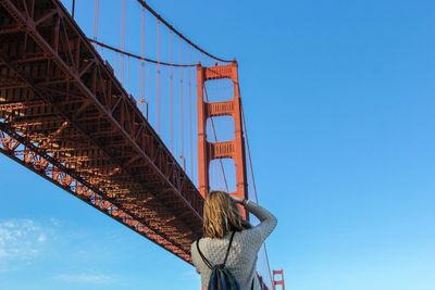 Rear view of woman photographing golden gate bridge against sky