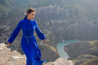 Brunette woman in a blue long dress stands on the edge of the sulak canyon in the evening at sunset