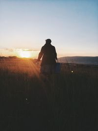 Rear view of woman walking on field during sunset