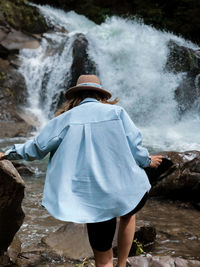 Rear view of woman standing on rock against waterfall