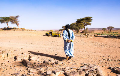 Rear view of man walking at desert against sky