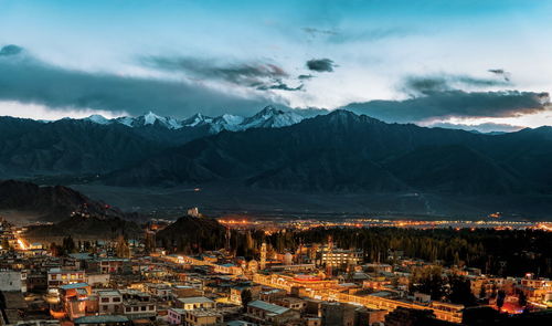 Aerial view of illuminated town by mountains against sky