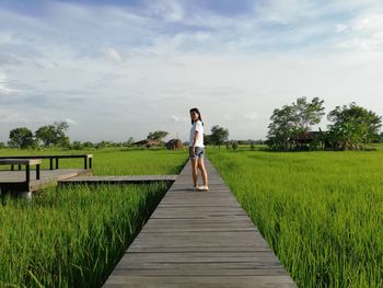 Man standing on footpath amidst field against sky