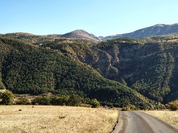 Scenic view of road by mountains against clear sky