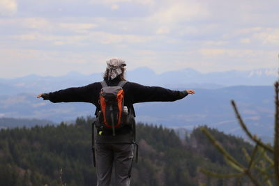 Rear view of man with arms outstretched against sky