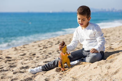 Little kid playing with a dinosaur on the beach