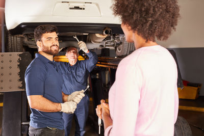 Mechanics repairing car while talking with customer