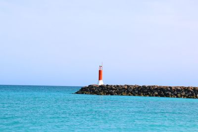 Lighthouse by sea against clear sky