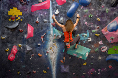 Back view of strong female athlete in sportswear clambering wall in modern bouldering center