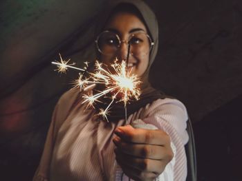 Close-up of woman holding sparkler at night