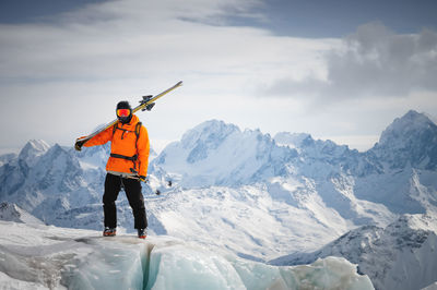 Portrait of a young skier with skis on his shoulder. it stands high in the mountains on a glacier