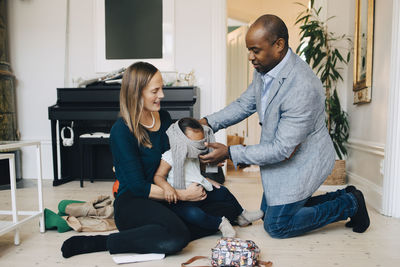 Parents dressing girl while sitting on floor in living room at home