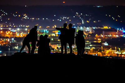 Silhouette people standing at illuminated park against sky at night