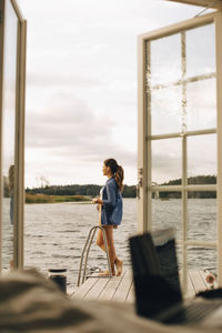 Full length of woman standing at patio against lake