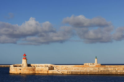 Lighthouse on building by sea against sky