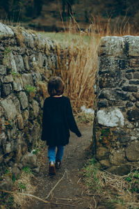 Rear view of girl standing by stone wall