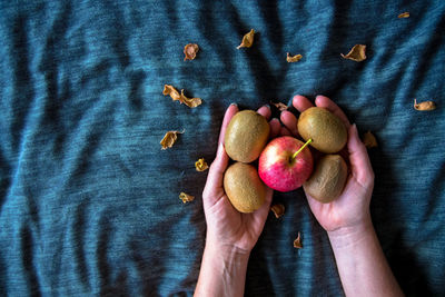 Cropped hands holding apple and kiwis on fabric