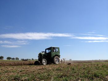 Tractor on grassy field against cloudy sky