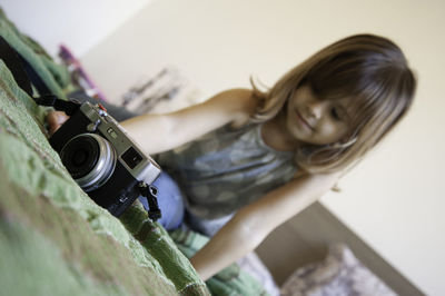 Cute girl sitting by camera on bed at home