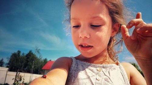 Cute girl with ladybug on hand against sky